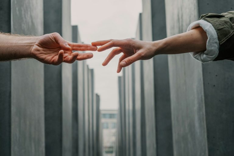 Trauma informed approach Two hands reaching out towards each other between tall concrete structures.