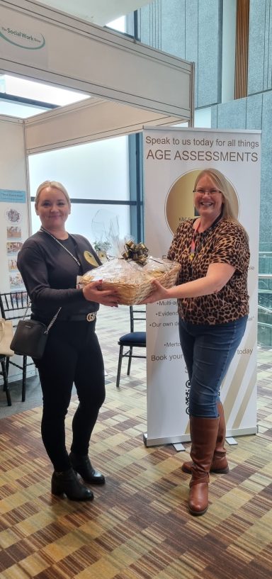 K&C raffle winner at The Social Work Show Two women hold a gift basket together, smiling in a bright indoor setting.