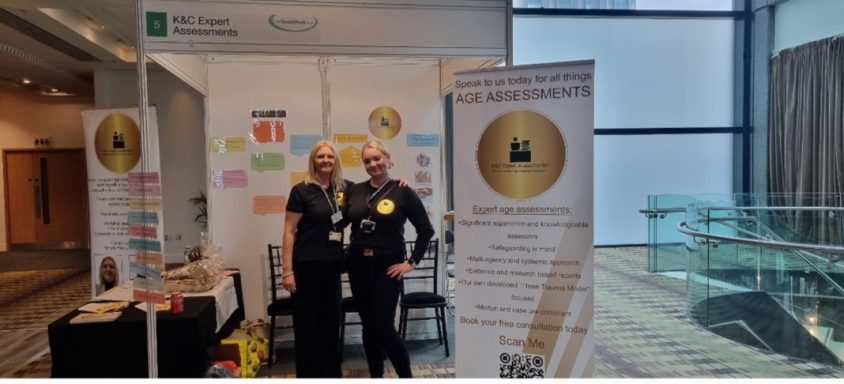 K&C Expert Assessments exhibiting at the Social Work Show Deansgate Manchester 2025 Two individuals in black attire stand at a promotional booth with various informational materials.